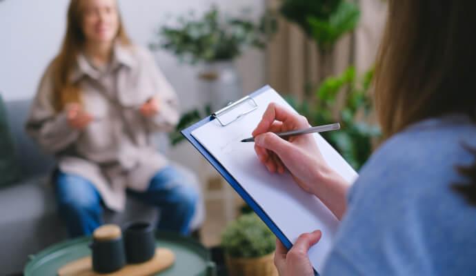 Two women sit facing each other. One is taking notes on a clipboard.