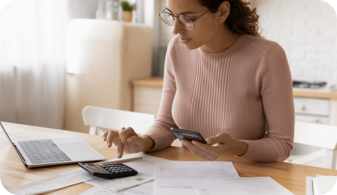 A female therapist uses her calculator while sitting at her laptop wondering about navigating private pay vs insurance clients