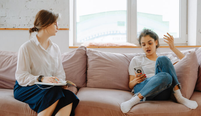 Two people are sitting on a couch. One of them is holding their phone, and looks irritated.