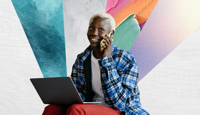 A young black woman sits on her laptop, talking on a cell phone.