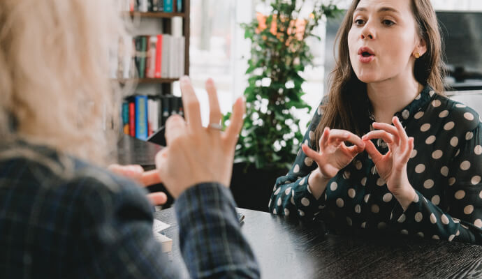 Two women sit opposite each other speaking in sign language.