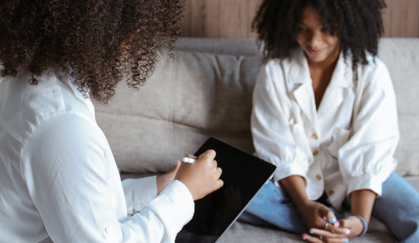 A female therapist with her adolescent client, writing a pediatric SOAP note on a tablet.